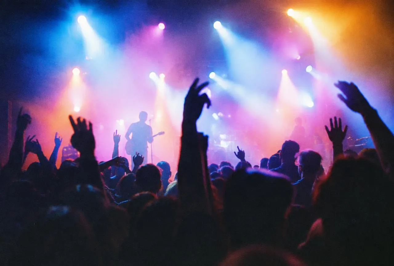 Concert crowd with hands raised under colourful stage lights