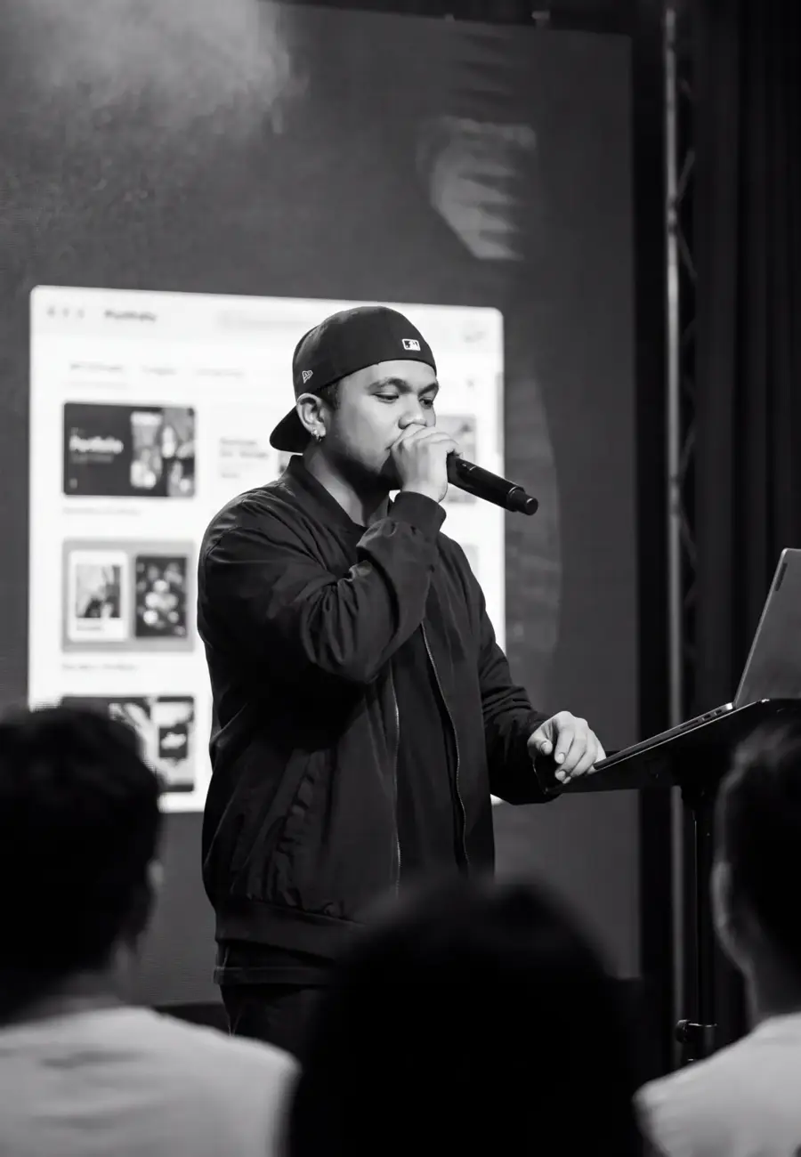 Black and white photo of Echo speaking on stage with a microphone beside a laptop