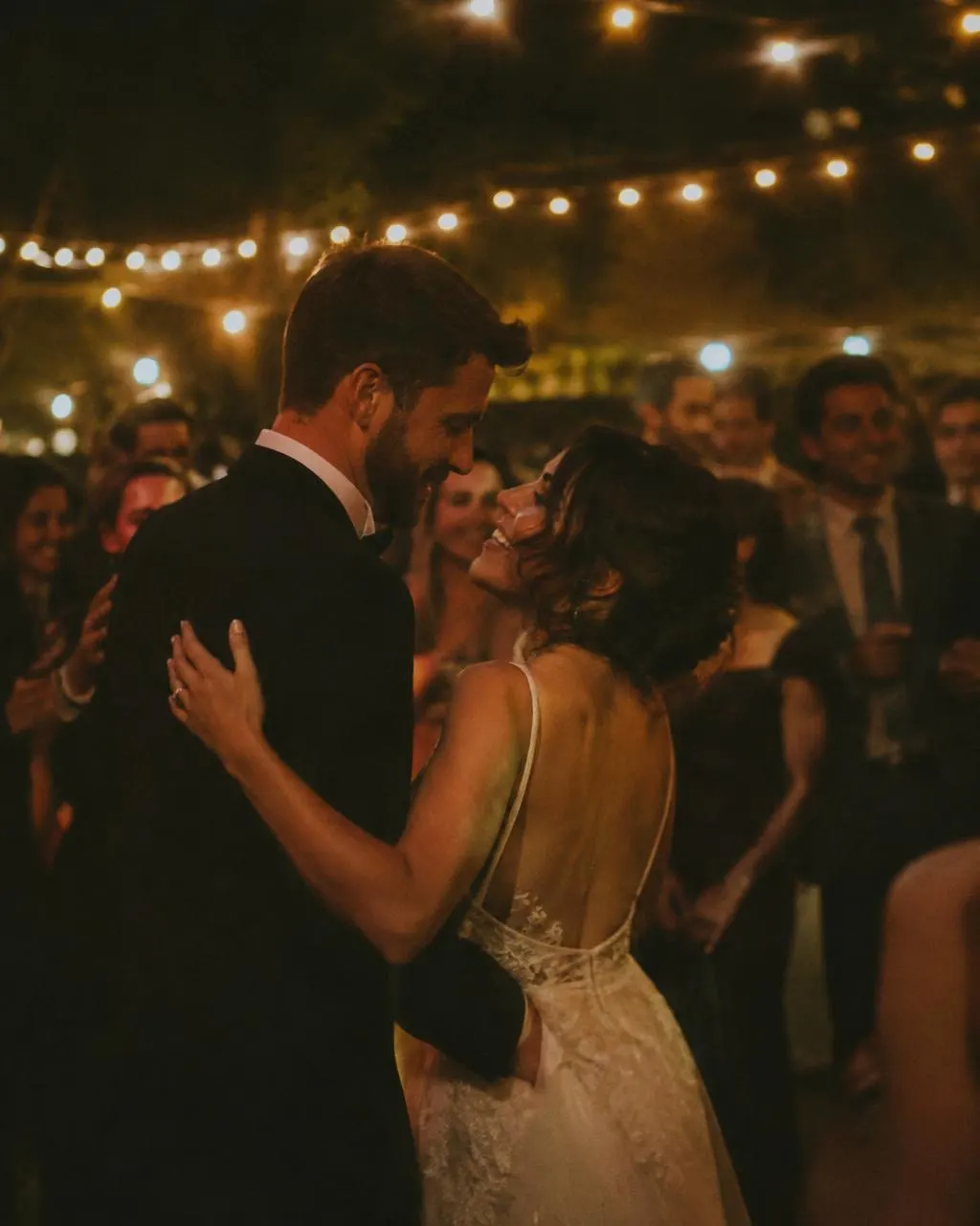 Couple sharing a first dance under string lights surrounded by guests